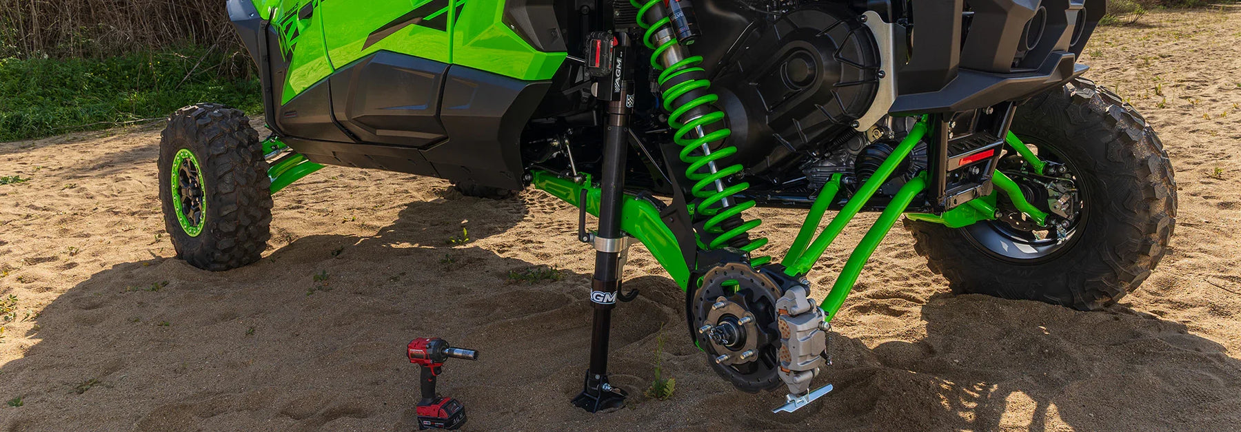 Close-up of a green off-road vehicle with suspension components being lifted by AGM Electric Jack PRO on sand surface