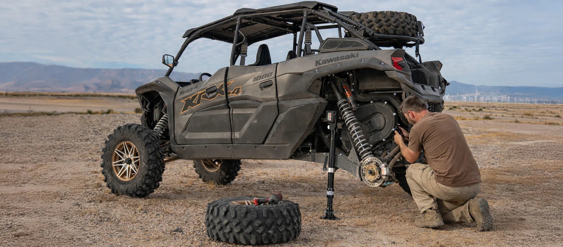 Person working on a Kawasaki KRX using AGM Electric Jack PRO to lift in the desert