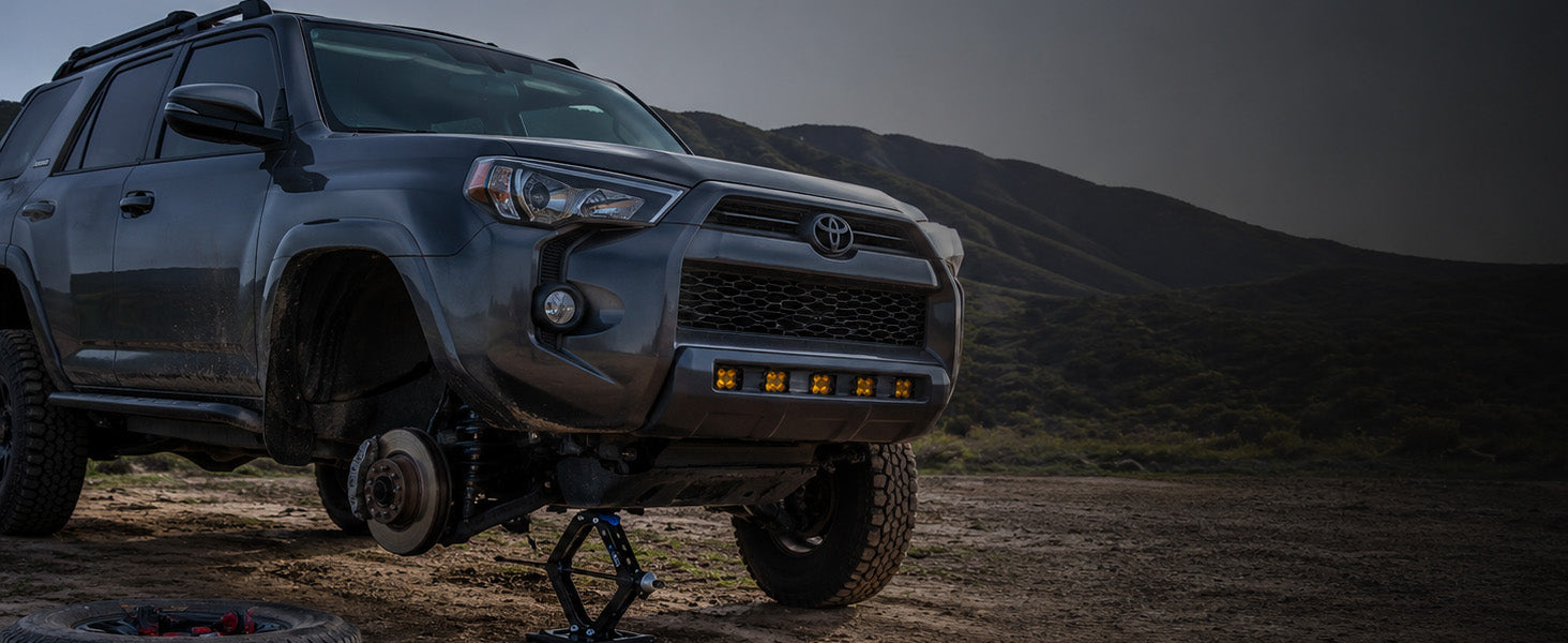 Toyota 4Runner in a desert landscape with mountains in the background being lifted by an AGM Scissor Jack HD