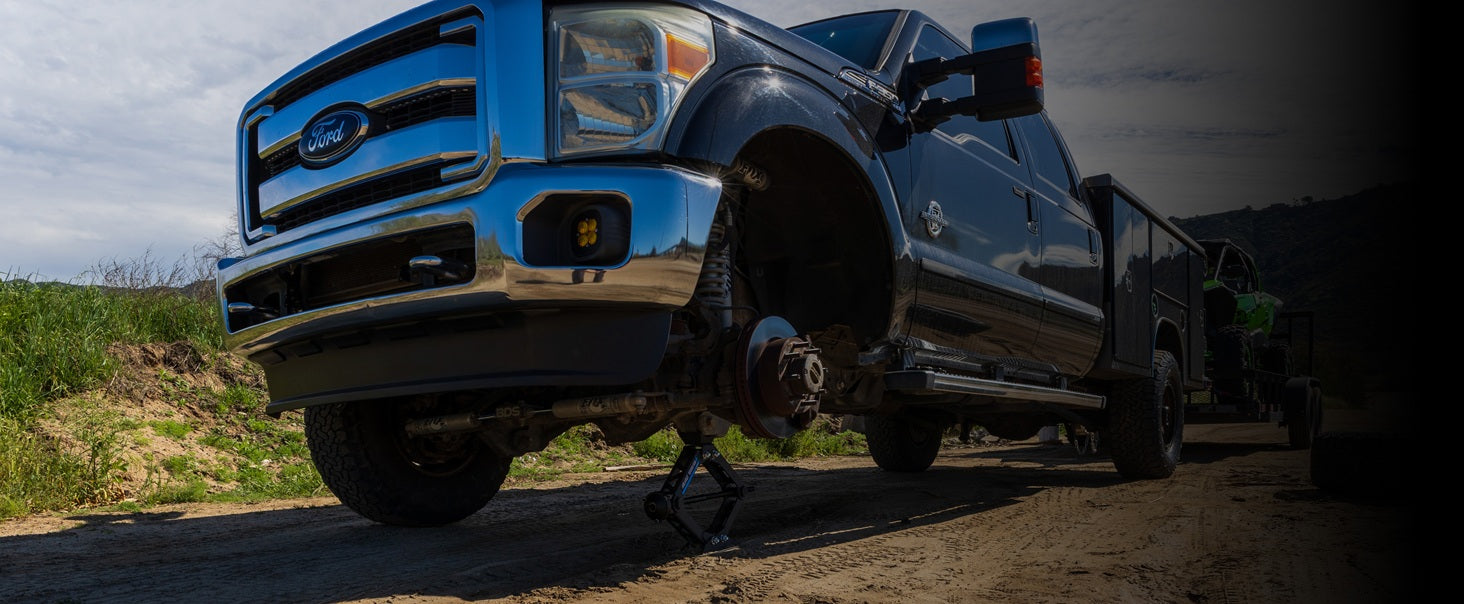 Ford truck towing a trailer on a dirt road being lifted by an AGM Scissor Jack HD