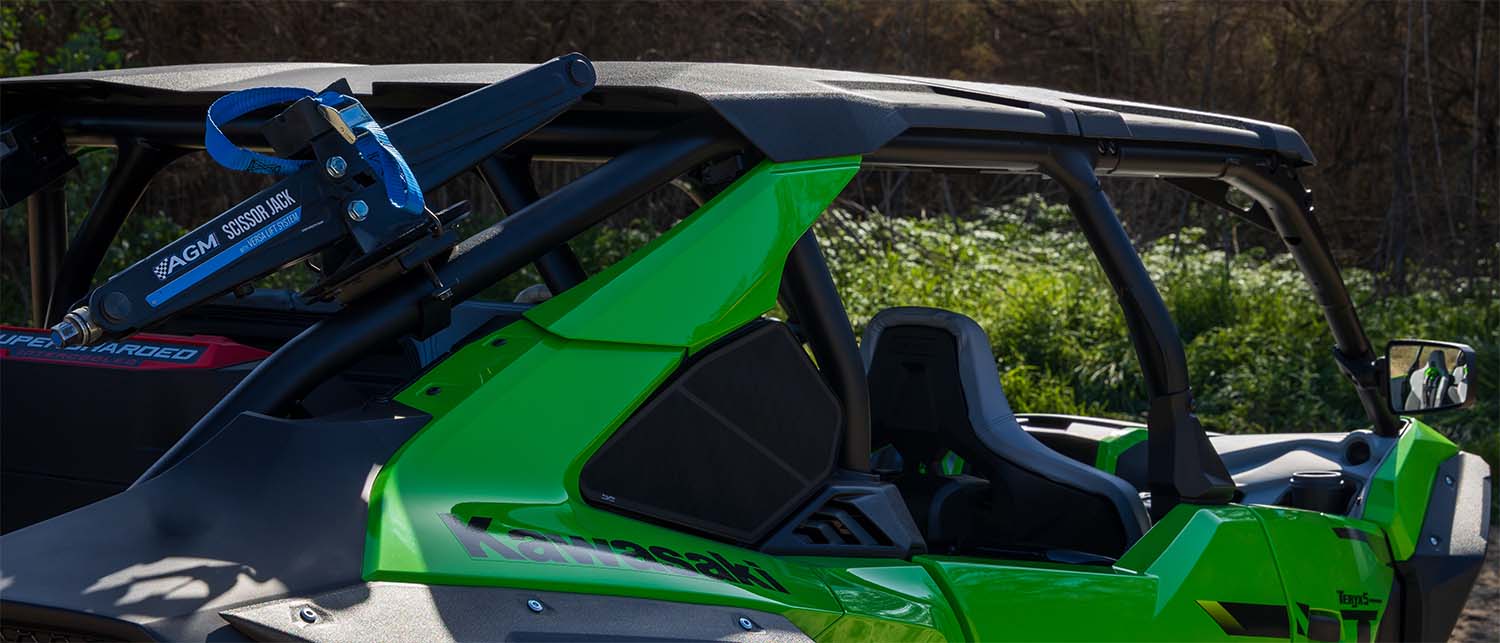 A bright green and black Kawasaki H2 SXS with a roll cage and side window, photographed outdoors in a grassy, wooded setting. An AGM Scissor Jack is mounted on the side frame.