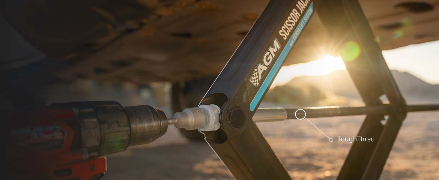 A close-up action shot of a cordless drill driving an AGM Scissor Jack, set against a blurred outdoor background with warm sunset light.
