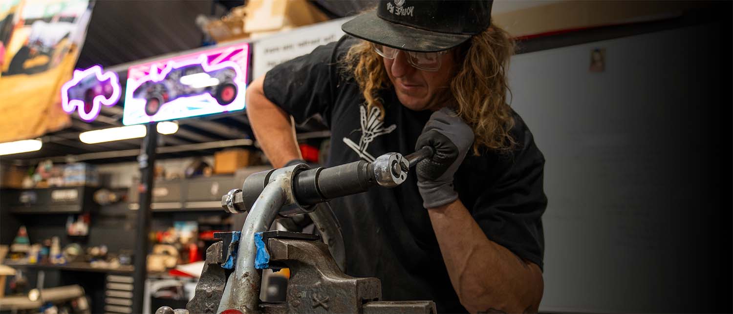 A man wearing a black cap, black t-shirt, and gray gloves remove a bearing with the AGM Uni-Ball Tool in a workshop.